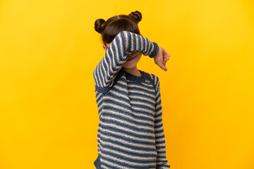 Little caucasian girl isolated on yellow background covering eyes by hands