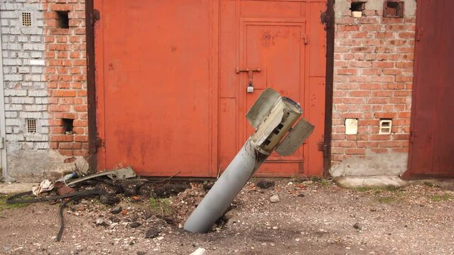 Close-up view 4k stock video footage of real unexploded military missile, torpedo or shell stuck in ground near doors of garages outdoors. Moments of dreadful war of Russia against Ukraine in 2022