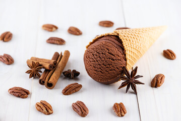 Chocolate ice cream in a waffle cone with cinnamon, pecan and anise on a wooden table.