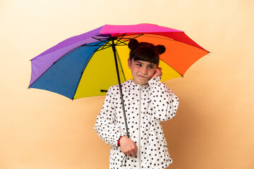 Little girl holding an umbrella isolated on beige background frustrated and covering ears