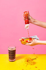Food pop art photography. Female hands tasting hotdog with dark beer isolated on bright pink and...