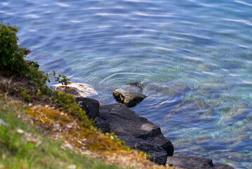 Fototapeta premium Lakeshore of Lake Geneva with rock and concentric waves and green blue colored water on a cloudy spring day. Photo taken April 4th, 2022, Montreux, Switzerland.
