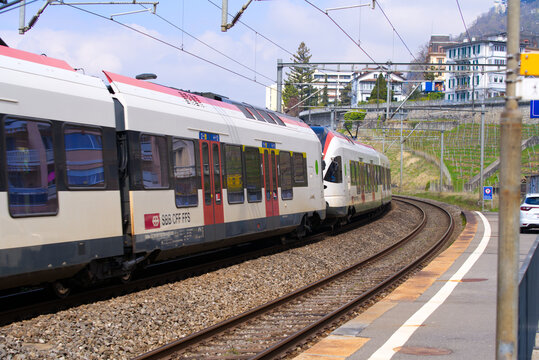 Regional RER train passing railway station Veytaux-Chillon on a blue cloud spring day. Photo taken April 4th, 2022, Veytaux, Switzerland.