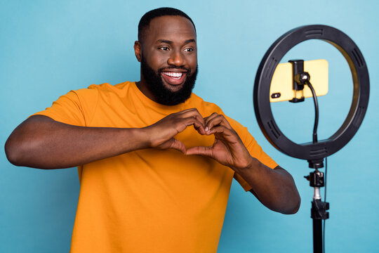 Portrait of handsome cheery guy recording video showing heart symbol isolated over bright blue color background
