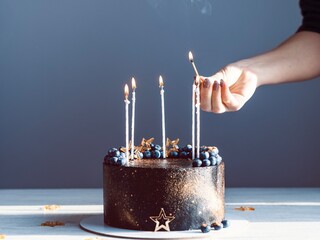 A girl lights candles on a cake with a match. Black and gold cake with candles
