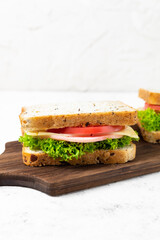 Two sandwiches with ham cheese tomatoes lettuce onions. Homemade sandwich with whole grain bread cutting board