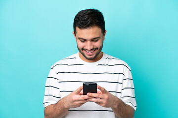 Young Brazilian man isolated on blue background sending a message or email with the mobile