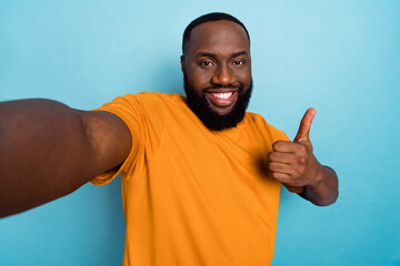 Photo of cheerful cool guy wear orange t-shirt recording self video thumb up isolated blue color...