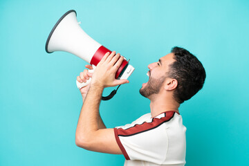 Young Brazilian man isolated on blue background shouting through a megaphone to announce something...