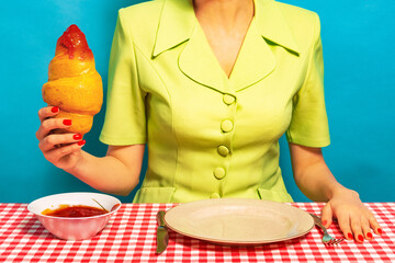 Food pop art photography. Cropped portrait of girl and fresh croissant on plaid tablecloth. Vintage, retro style interior