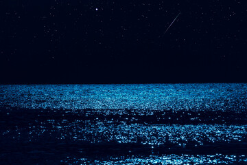 Moonlight reflection with starry skies above ocean horizon.