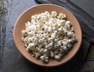Photo with popcorn was made in a rustic setting with a handmade clay container on stone called slate.