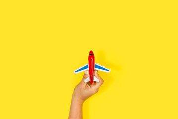 Mano de mujer sosteniendo un avión de juguete sobre un fondo amarillo liso y aislado. Vista de...