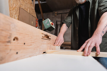 partial view of joiner working with timber on jointer machine.