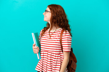 Student teenager redhead girl isolated on blue background laughing in lateral position