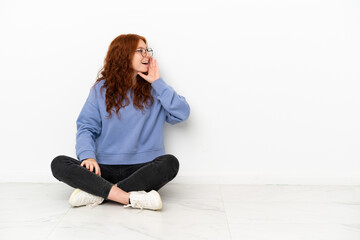 Fototapeta na wymiar Teenager redhead girl sitting on the floor isolated on white background shouting with mouth wide open to the lateral