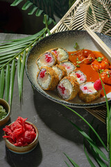 Tempura sushi rolls with bright filling among the greenery of a palm tree on a gray plate