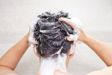 Male hand washes his head with shampoo and foam on gray background close-up, back view. - obrazy, fototapety, plakaty