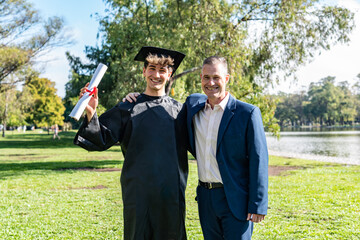Portrait of a happy caucasian graduated young man with his father on his graduation day.  They are...