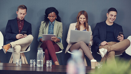 Even while they wait, they manage to do work. Shot of a group of businesspeople using different...