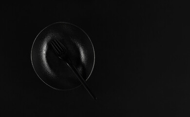 Elegant black plate in the japanese style with fork, table setting. Flat lay. Black background. Minimalist breakfast idea in black color.