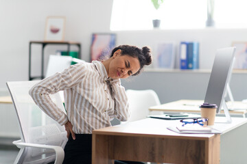 Fototapeta na wymiar Tired businesswoman suffering from back and neck pain, muscle spasm at workplace in office interior