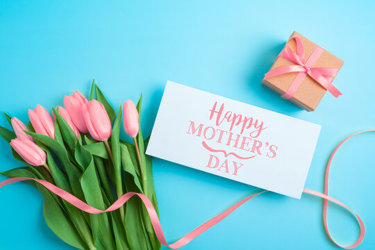 Happy Mother's day concept with greeting card, gift box and beautiful tulip flowers on blue background. Flat lay, top view