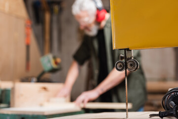 selective focus of band saw near carpenter working on blurred background.
