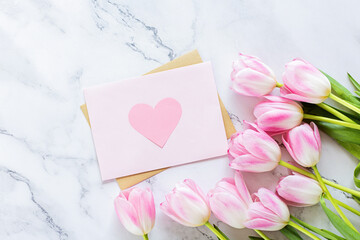 Greeting card for spring holiday, pink tulip flowers lying on white marble background with copy space. Flat lay top view Template for Mother's Day.