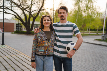 Couple woman and young caucasian man modern happy adult male and female boyfriend and girlfriend smile portrait waist up holding soccer ball walking together outdoor football concept copy space