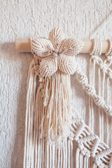 Handmade macrame wall decoration with wooden stick hanging on a white wall. Macrame braiding and cotton threads. Female hobby. ECO friendly modern knitting natural decoration in interior