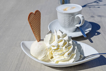 Ice cream dessert with whipped cream and cookieon a plate and a cup of coffee on a table outdoors...