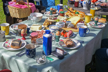 Large table set at a casual outdoor Easter brunch with family and many guests full of food in the garden on a sunny day, selected focus