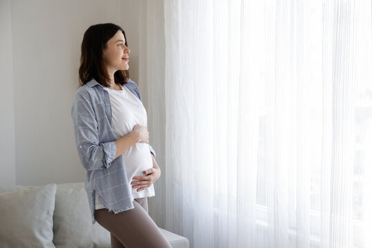 Young beautiful woman on second trimester of pregnancy. Close up of pregnant female in yoga pants with arms on her round belly. Expecting a child concept. Background, copy space.
