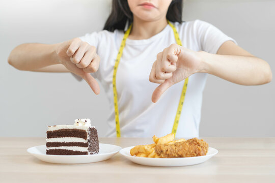 Diet, Dieting unhealthy asian young woman, girl hand in deny, rejecting chocolate cake or sweet taste and fried chicken, french fries or junk food. Nutritionist of healthy, nutrition of weight loss.