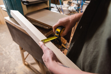 cropped view of furniture designer measuring plank while working in woodwork studio.