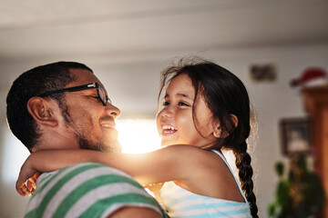 My little girl. Shot of a cheerful little girl being held in her fathers arms inside at home during...