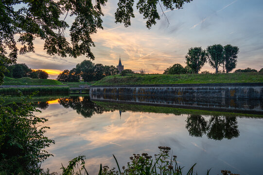 Beautiful orange sky during sunset with a reflection and church in Naarden Vesting, The Netherlands, stock photo, Holland, Naarden