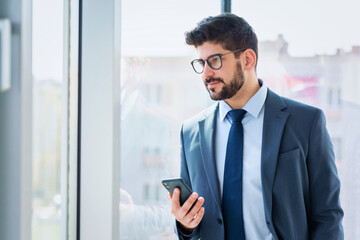 Confident businessman text messaging while standing by the window at the office