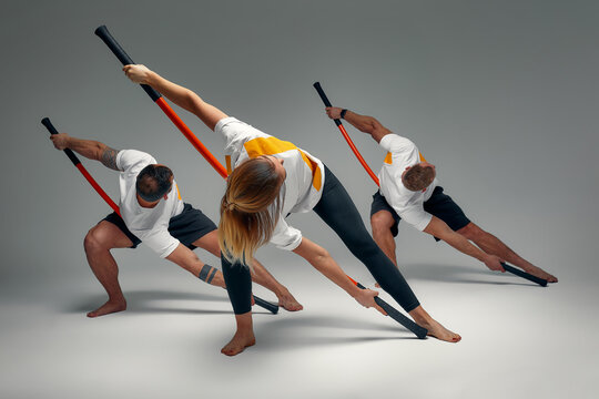 Two men and woman aikido fighters with wooden fight stick posing in studio, fight demonstration