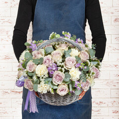 Young women florist in denim apron holding bunch of flowers over brick wall