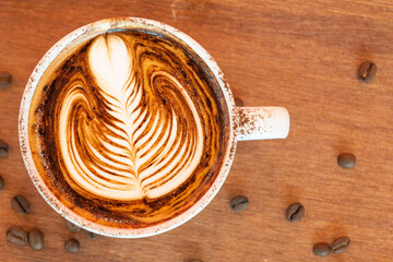 Latte art coffee cup on glass table. Blurred leaf reflection background.