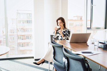 Attractive businesswoman relaxing at office desk and drinking her morning coffee