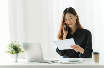 Asian businesswoman in formal suit in office happy and cheerful during using smartphone and working with financial report.