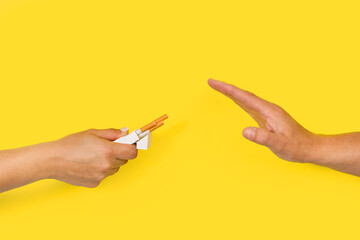 Mano de mujer con un paquete de cigarrillos y mano de hombre negandose a aceptar sobre un fondo amarillo.  Vista de frente y de cerca. Copy space. Concepto: Salud, tabaquismo - obrazy, fototapety, plakaty