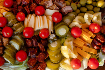 cherry tomatoes, sweet peppers,  pickled cucumbers, pickled garlic, olives,  sausage, different cheese, bacon on wooden plate. Snack food