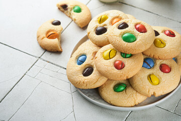 Homemade cookies with colorful chocolate candies and milk. Stack of shortbread cookies with multi colored candy on plate with bottle of milk on light gray background. Baby food concept. Copy space.