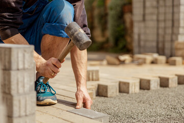 Young man laying gray concrete paving slabs in house courtyard on gravel foundation base. Master...