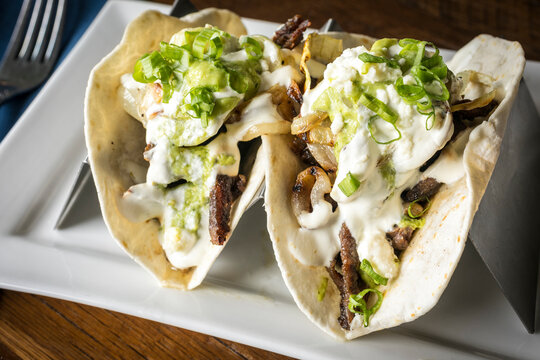 Close Up of Two Steak Tacos with Lettuce, Sour Cream, and Cotija
