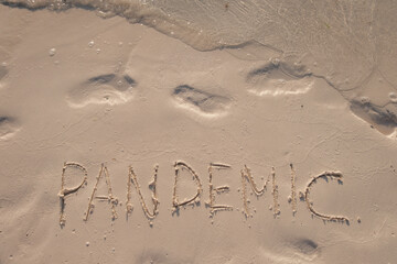 Pandemic. Handwritten text on smooth sand beach